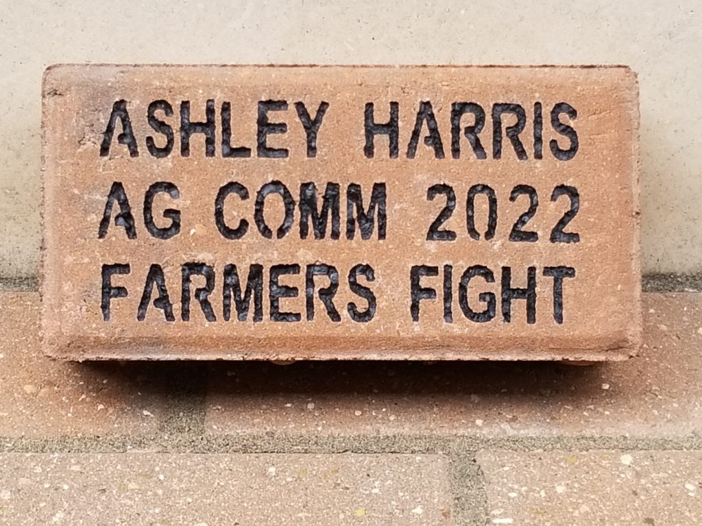 A brick with "Ashley Harris, Ag Comm 2022, Farmers Fight" engraved.