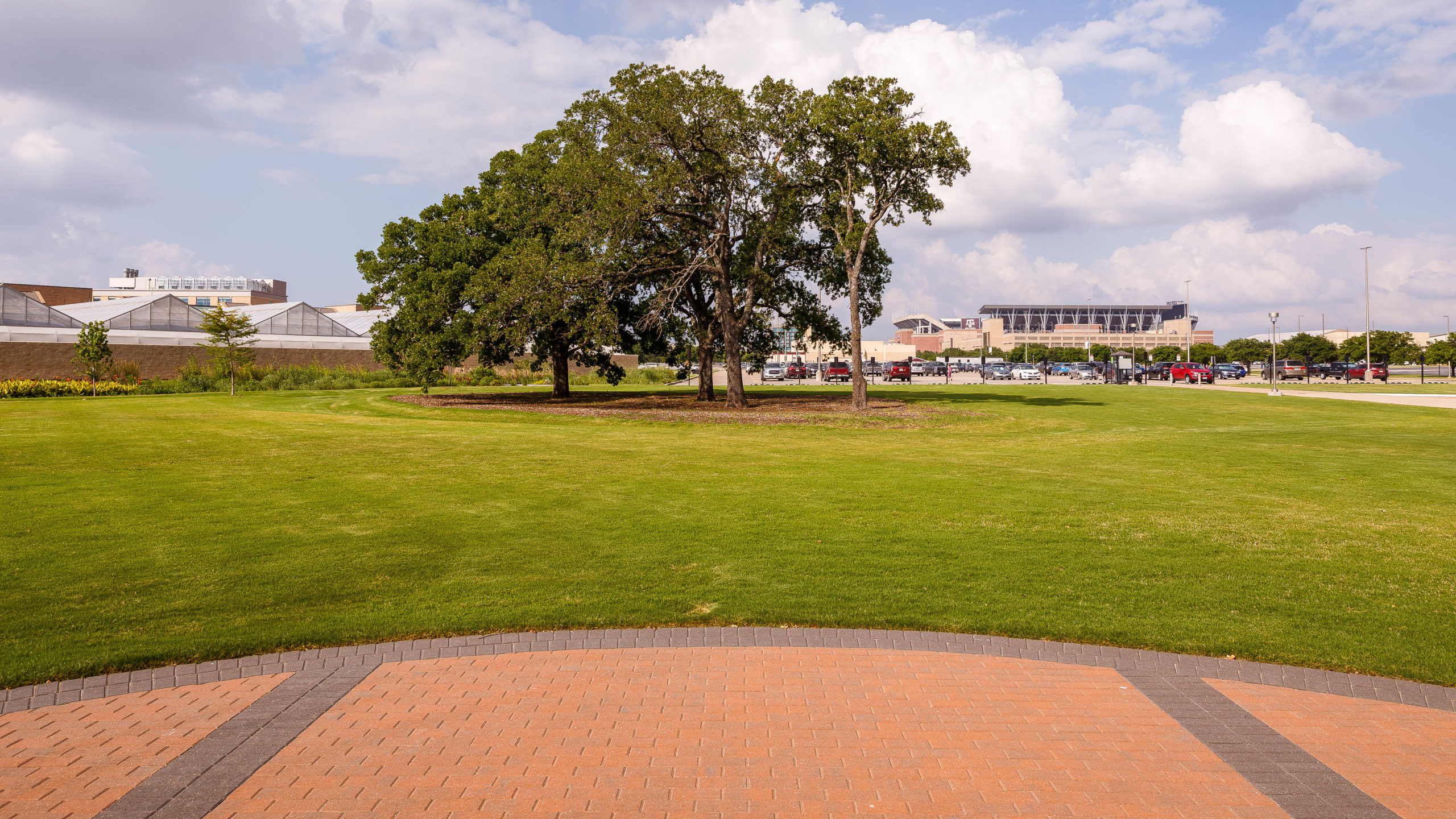 A photo facing the trees, parking lot, greenhouses, and Kyle Field beside The Gardens.