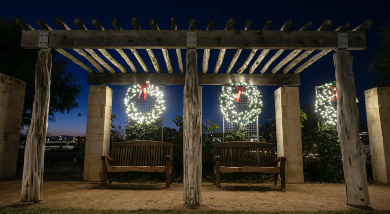 A picture of two benches with two wreaths decorated in holiday lights above them