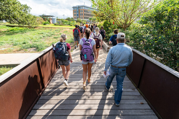 College students walking across a bridge as part of a tour at The Gardens.