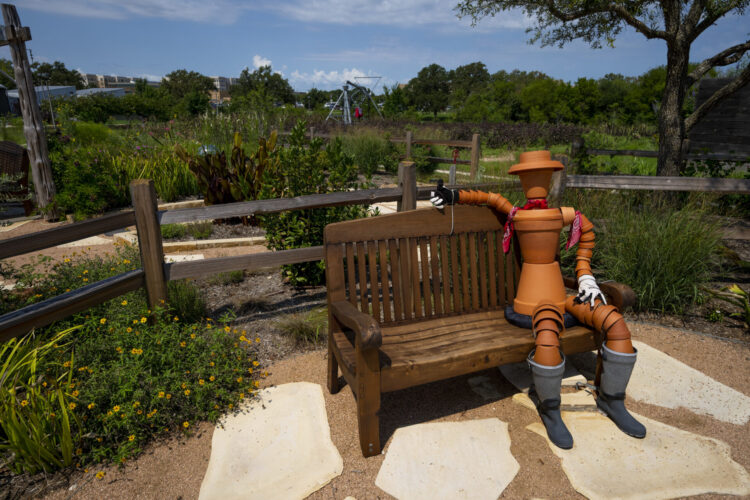terra cotta pot sculpture sits on a bench in front of the cottage garden