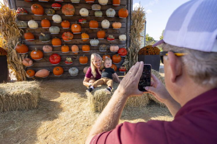 Grandparent and child pose in front of the garden's pumpkin selfie wall.